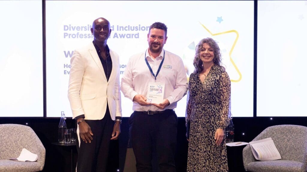 Winner of the Diversity and Inclusion Professional Award holding trophy on stage with two presenters at the Disability Smart Impact Awards.