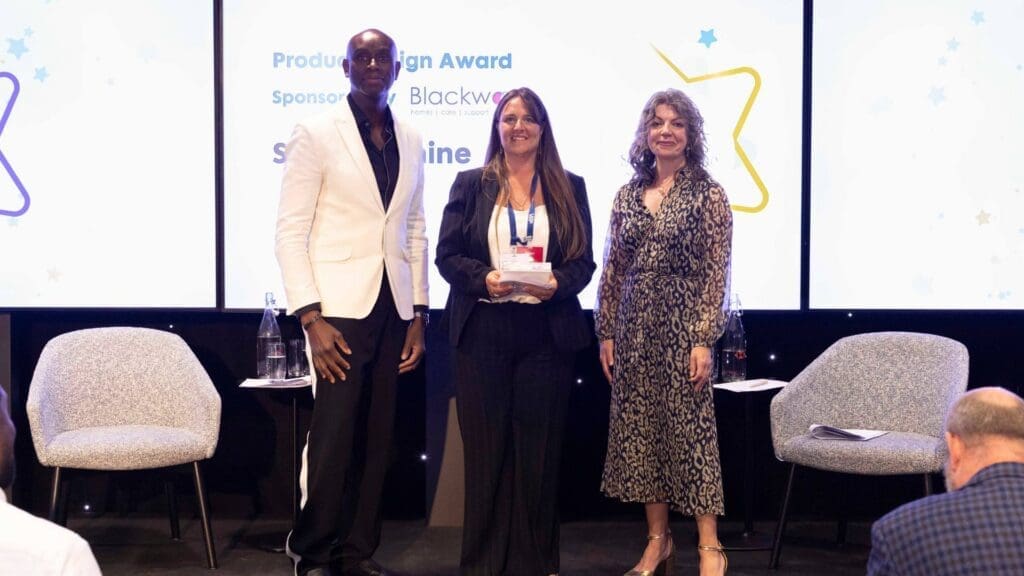 Sensory Shine representative holding Product Design Award on stage with presenters at the Disability Smart Impact Awards 2026.