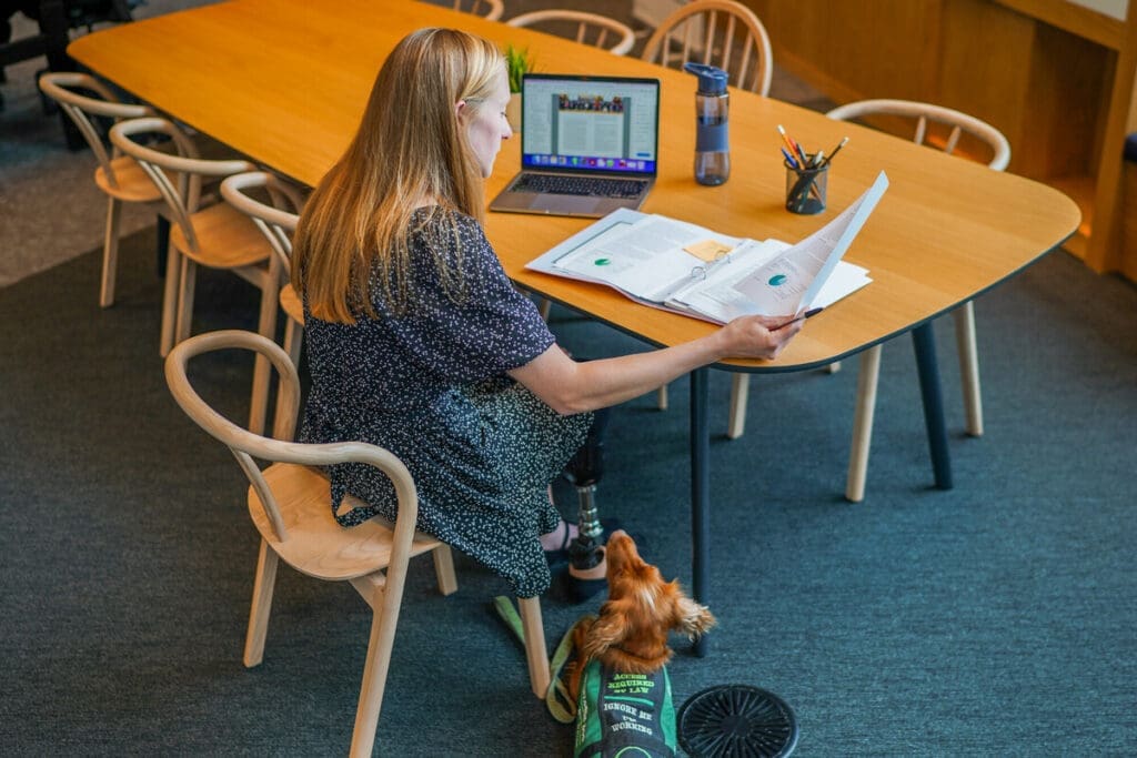 Person with prosthetic leg studies notes at table with assistance dog