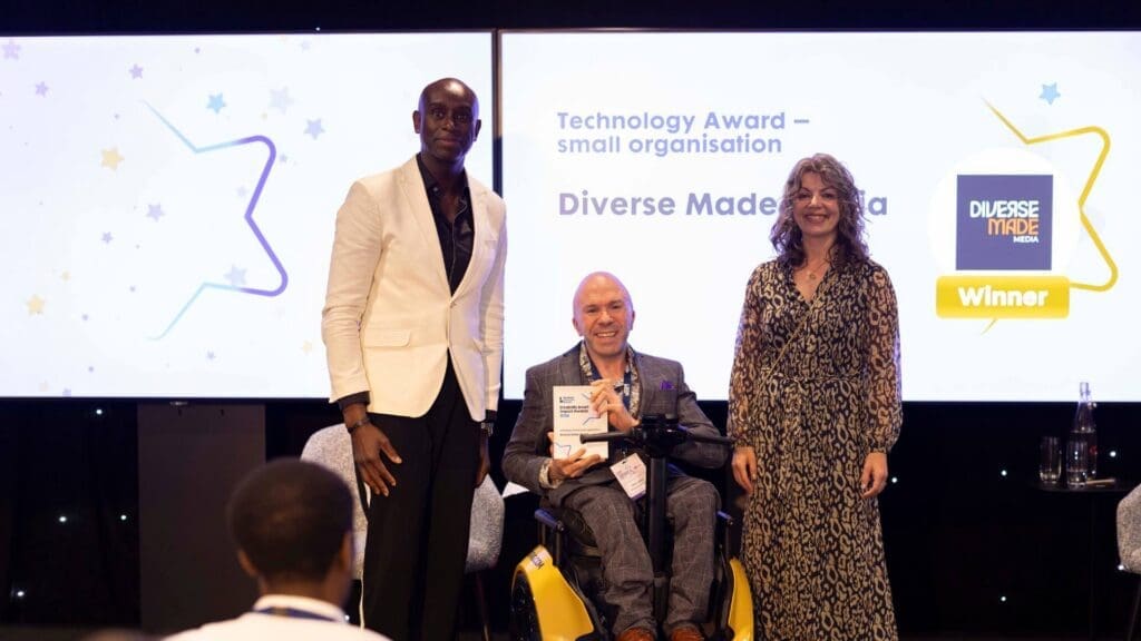 Diverse Made Media winner holding Technology Award while seated in a powered wheelchair on stage at the Disability Smart Impact Awards 2026.