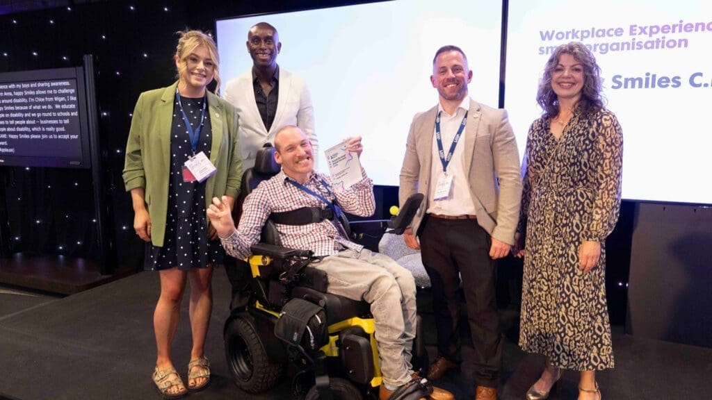 Happy Smiles team celebrating award win on stage, including a wheelchair user holding the trophy at the Disability Smart Impact Awards 2026.