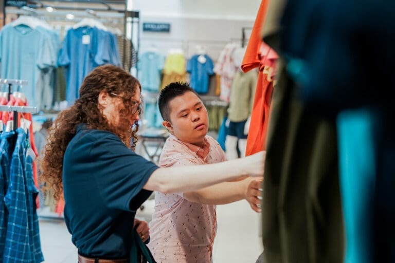 Shop assistant helps a customer with Down's Syndrome with some clothes in a shop.